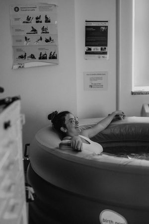 A birthing pool scene in black and white with instructional posters visible on the wall in a medical setting.