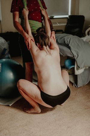 Physical therapy or stretching session with someone assisting another person with exercises on the floor.