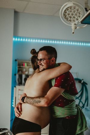 A supportive moment during labor as two people share an emotional embrace in a medical room with blue lighting.