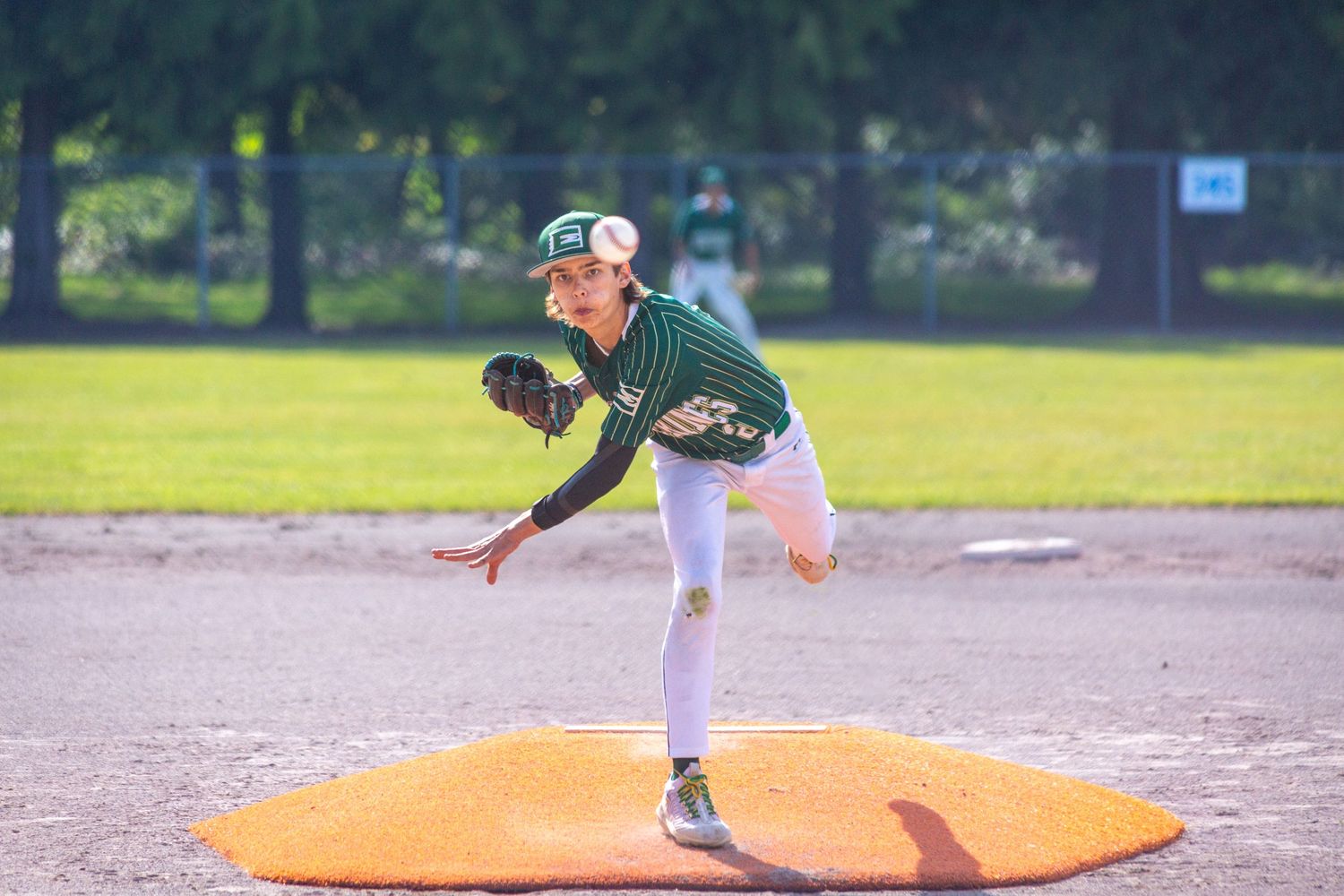 Baseball pitcher in green jersey follows through on delivery from pitching mound during game.