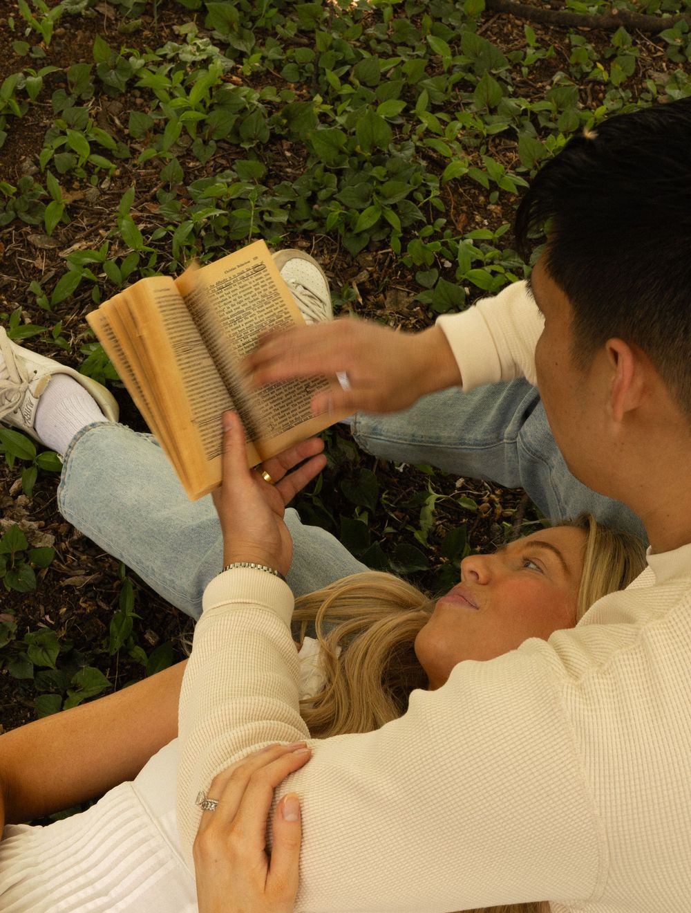 Two people relaxing outdoors on green grass while sharing a book together on a peaceful afternoon.