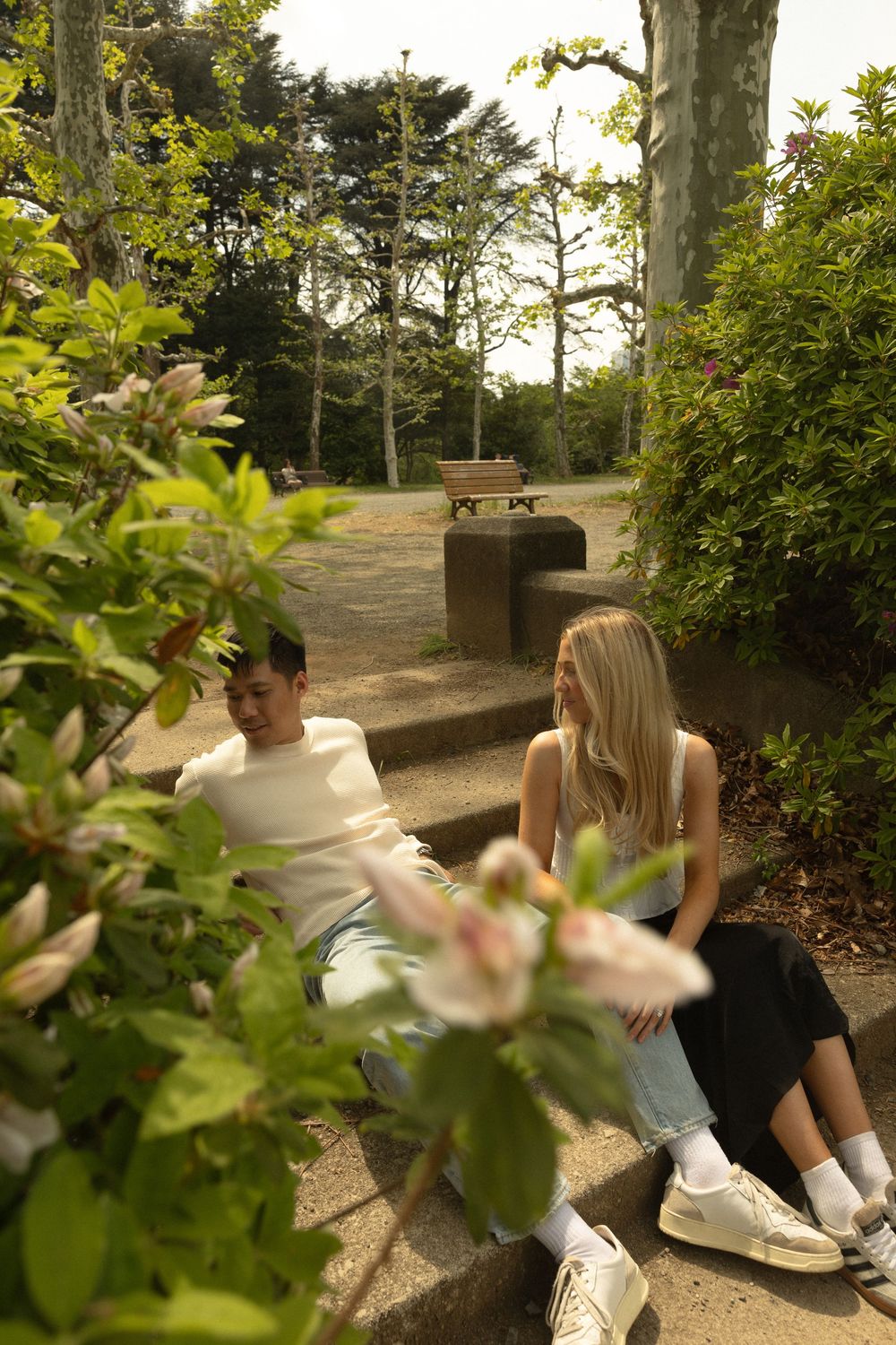 A couple sits together on garden steps surrounded by lush greenery and bushes.