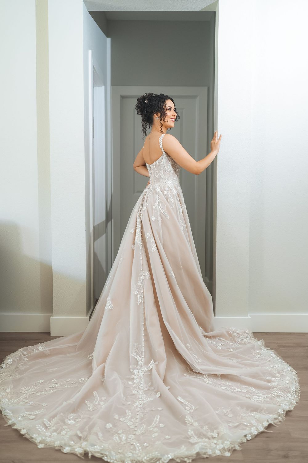 Back view of wedding gown with detailed lace train and elegant silhouette in hallway.