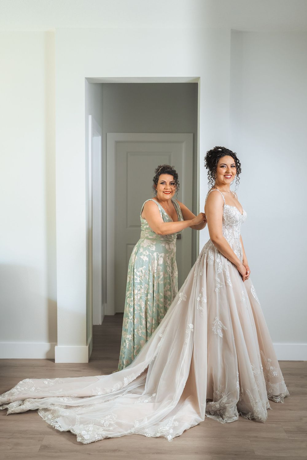 Two women share a tender moment during wedding dress fitting with a beautiful lace gown and train.