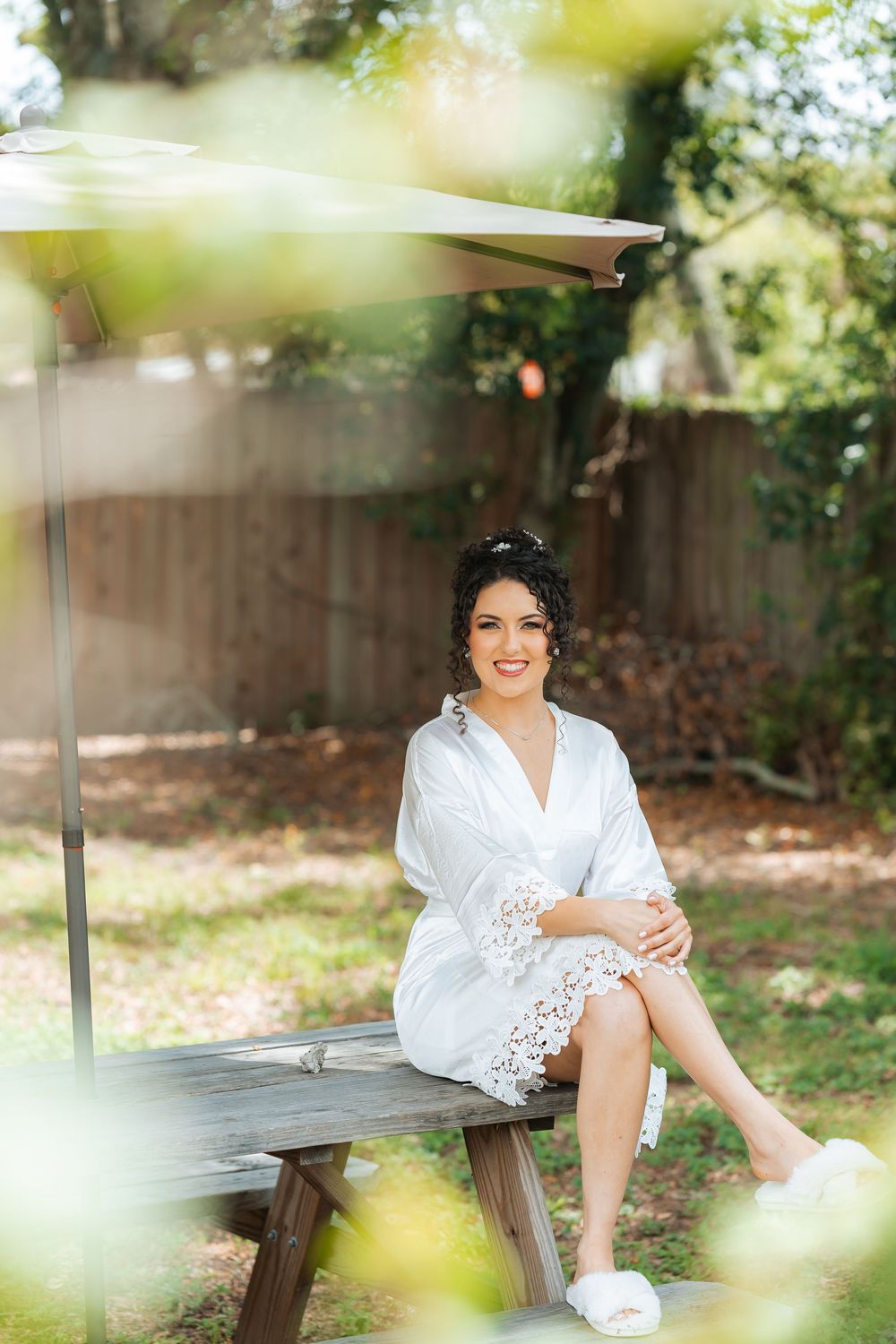 Woman in white lace robe sitting on wooden bench in sunlit garden setting.