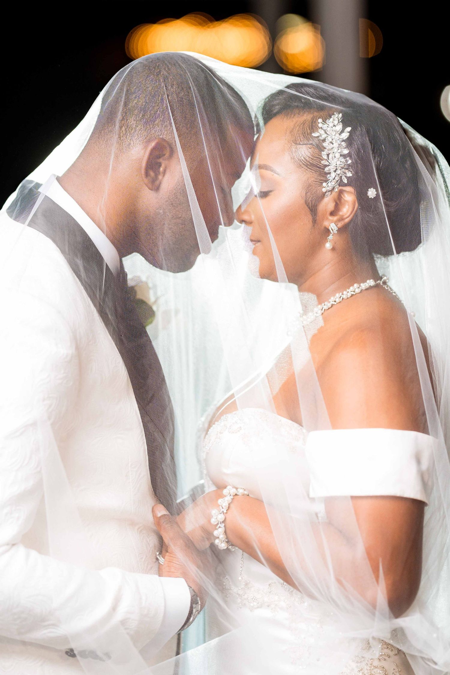 A tender wedding moment captured under veils as newlyweds share an intimate pose in elegant white attire.