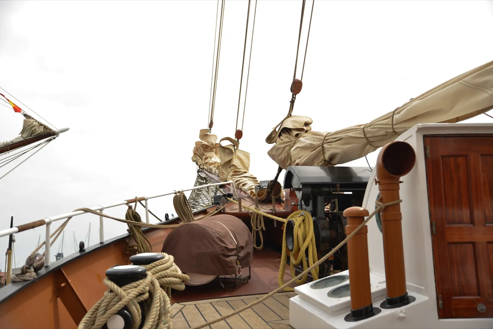 Détails du pont d’un voilier classique avec poulies, voiles pliées et équipements nautiques, capturant une esthétique marine authentique.