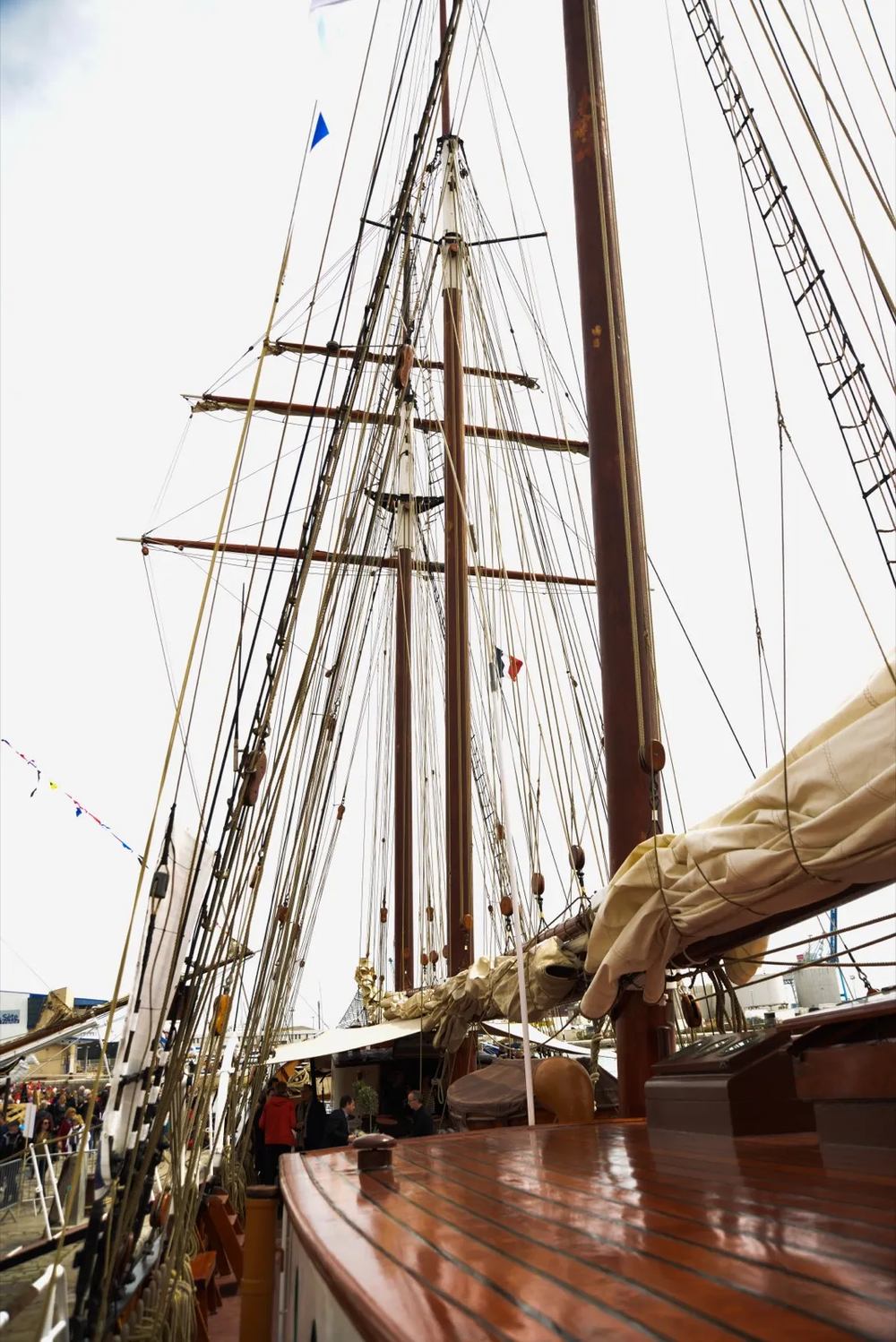 Contre-plongée sur les mâts imposants d’un grand voilier en bois, avec les cordages tendus et les voiles enroulées.