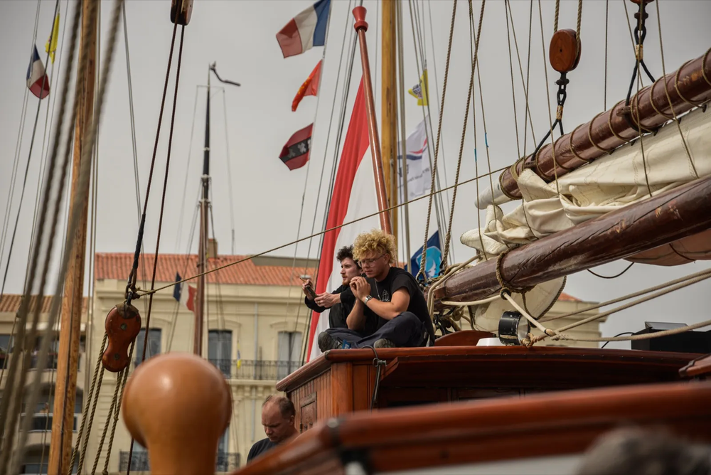 Une femme souriante assise sur le pont d’un bateau ancien, entourée de mâts et de drapeaux colorés, dans une ambiance de fête maritime.