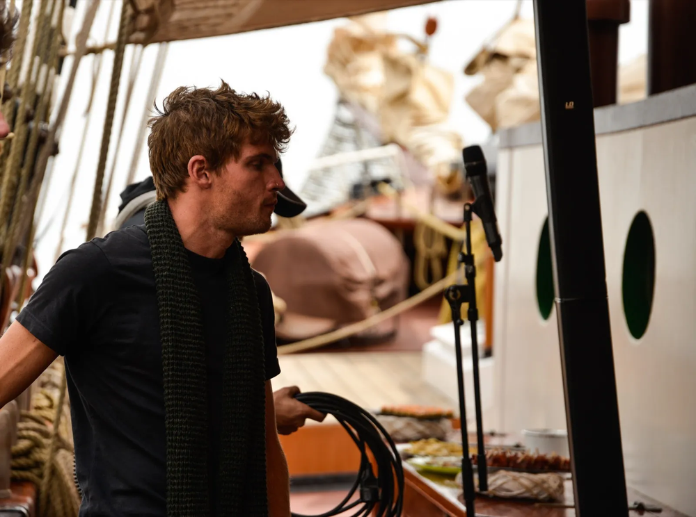 Un musicien accoudé à la rambarde d’un bateau, regard concentré, tenant une guitare entre deux morceaux.