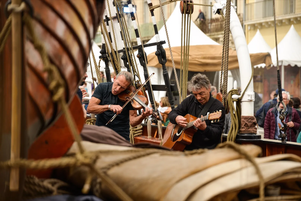 Scène musicale à bord d’un voilier ancien, avec un groupe concentré sur leur performance au milieu des voiles et poulies.