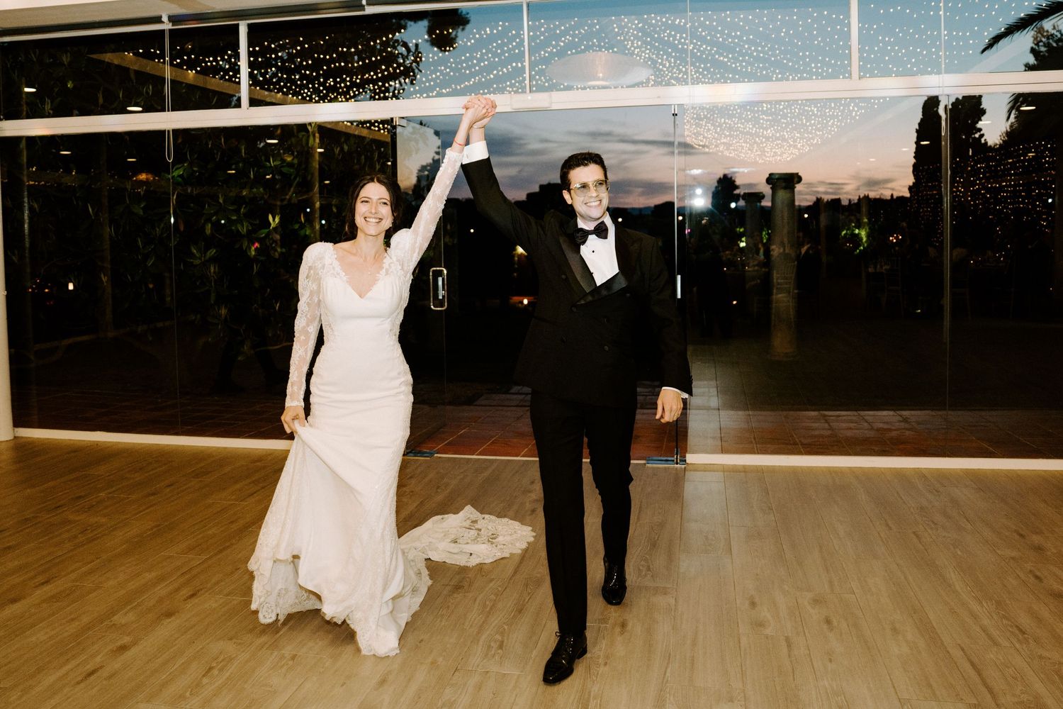 A couple performs their first dance in an elegant ballroom with floor-to-ceiling windows.