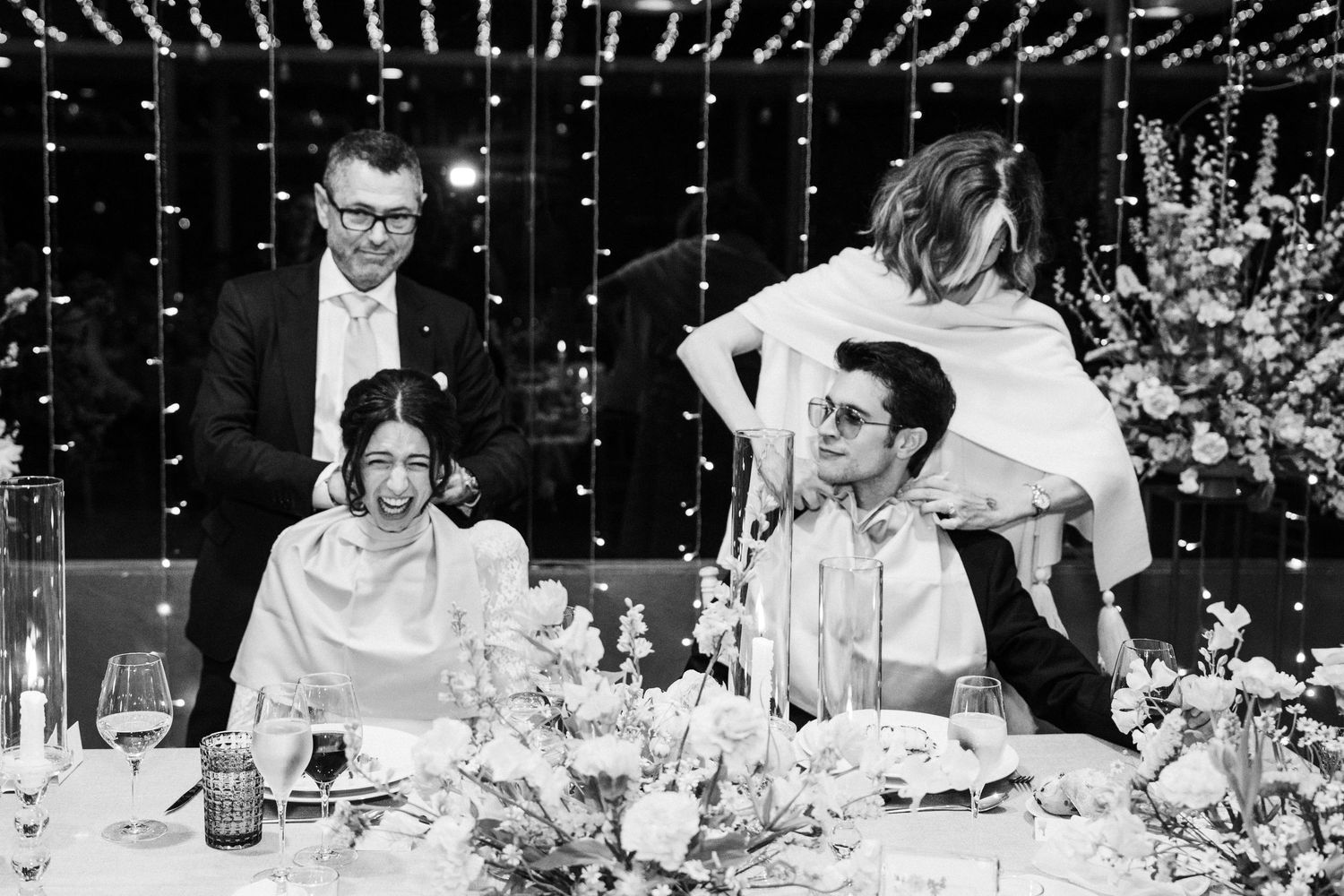 Black and white photo of wedding guests enjoying dinner and speeches at reception tables.