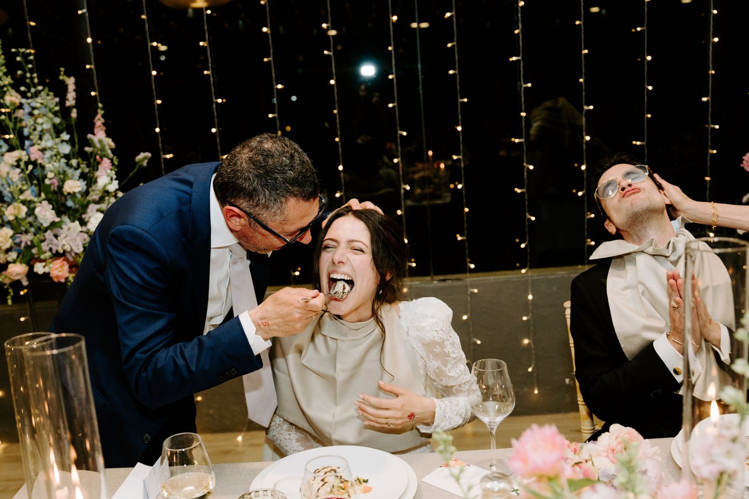 Wedding reception venue with romantic string light backdrop and floral table settings.