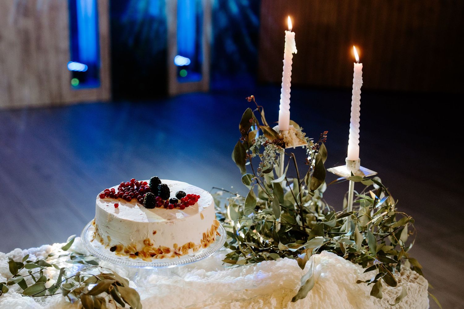 White wedding cake decorated with greenery and candles in an elegant display setting.