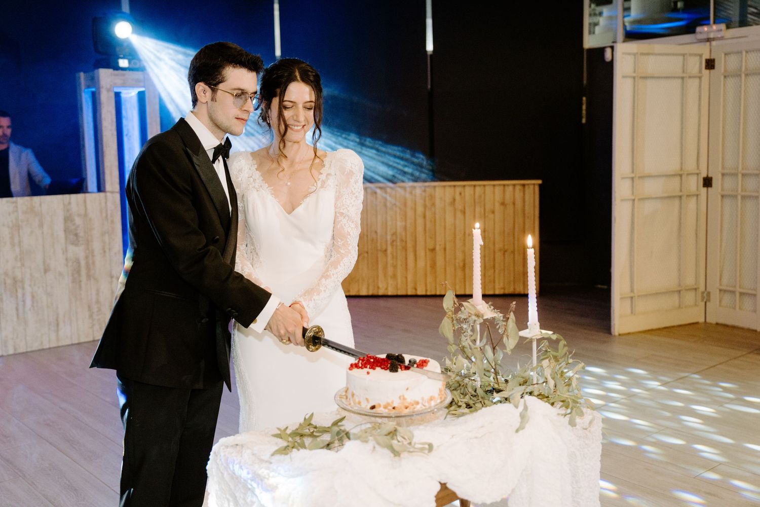 Couple cutting their wedding cake together in a beautifully lit reception venue.