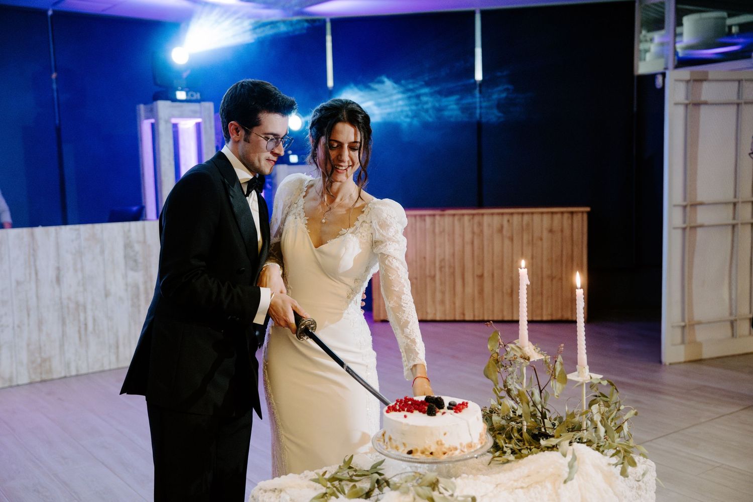 Newlyweds sharing a moment during their cake cutting ceremony under blue ambient lighting.