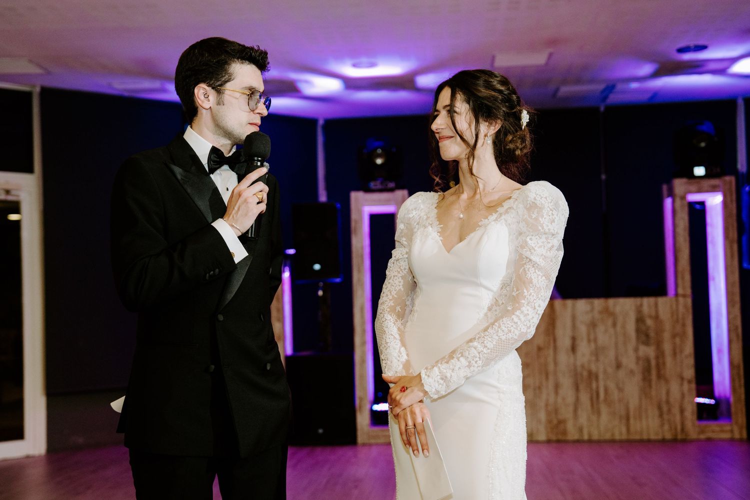 A couple performs an elegant dance move on a dimly lit dance floor with purple and blue lighting.
