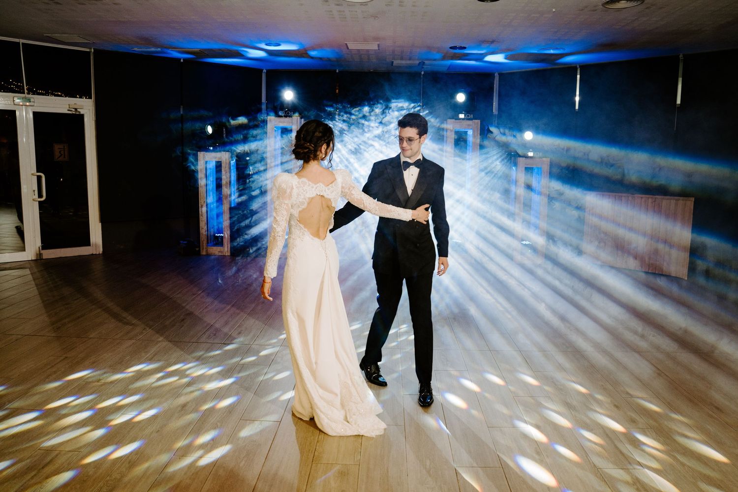 Dancers move gracefully across a wooden floor under dramatic lighting during a formal event.