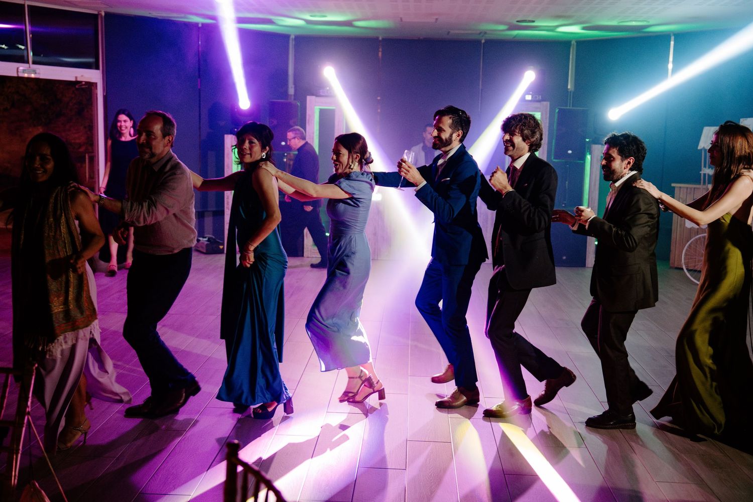 Dance floor filled with party guests under vibrant purple and green lighting effects.