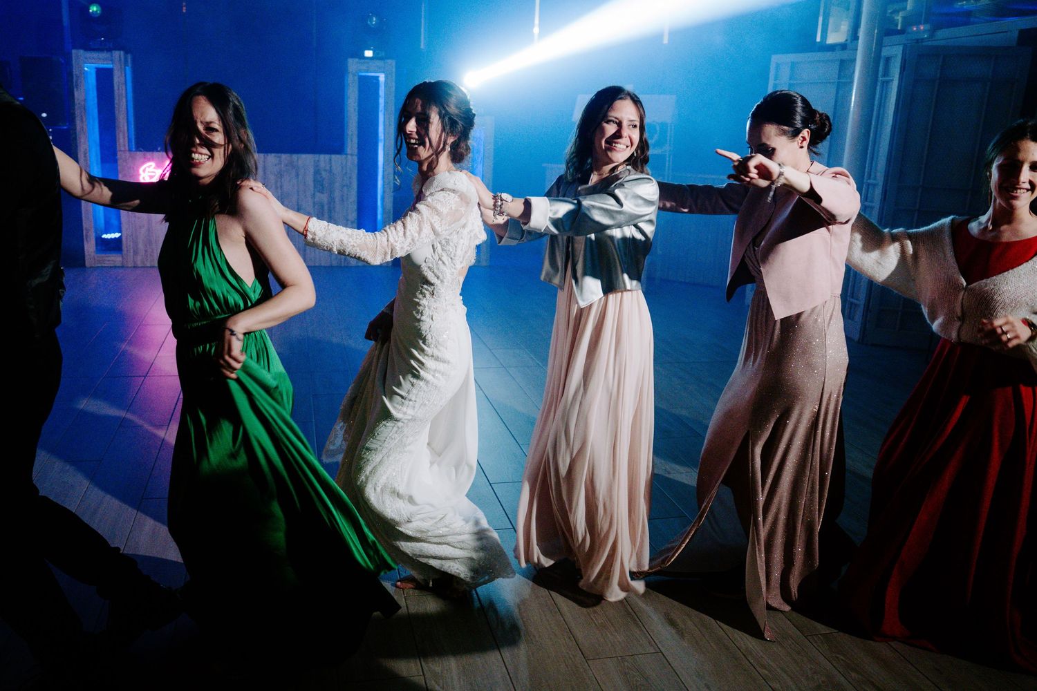 Wedding party line dance under blue atmospheric lighting in an indoor venue.