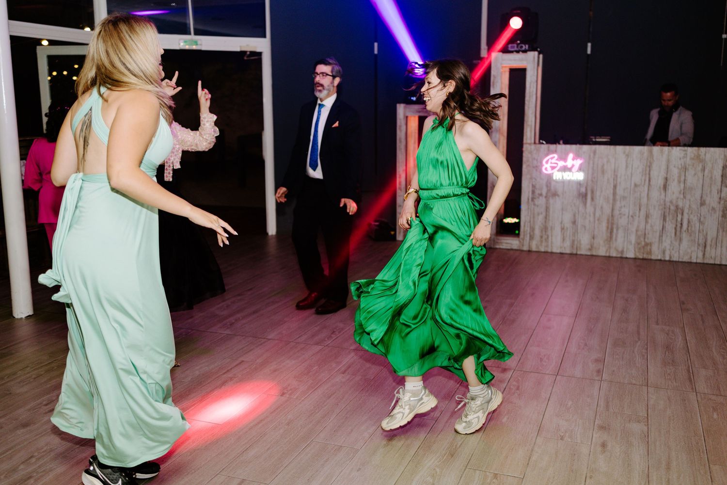 Wedding reception dancers in colorful dresses moving under dramatic lighting effects.
