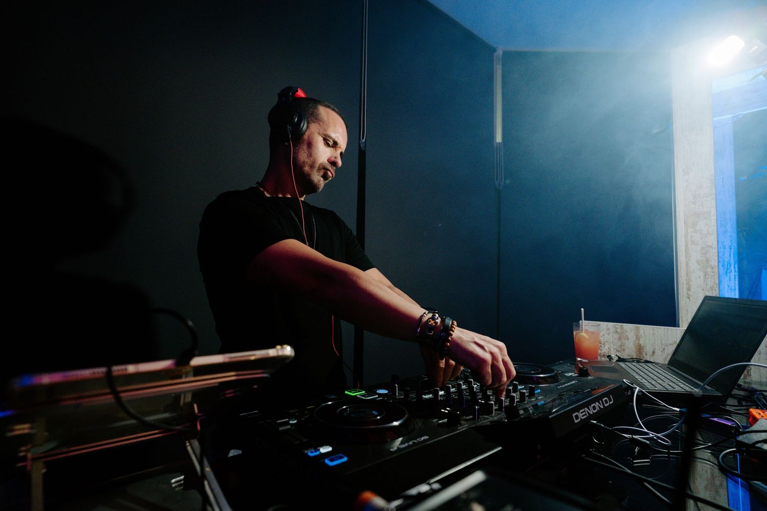 DJ performing in a dark room with blue lighting and professional equipment setup.