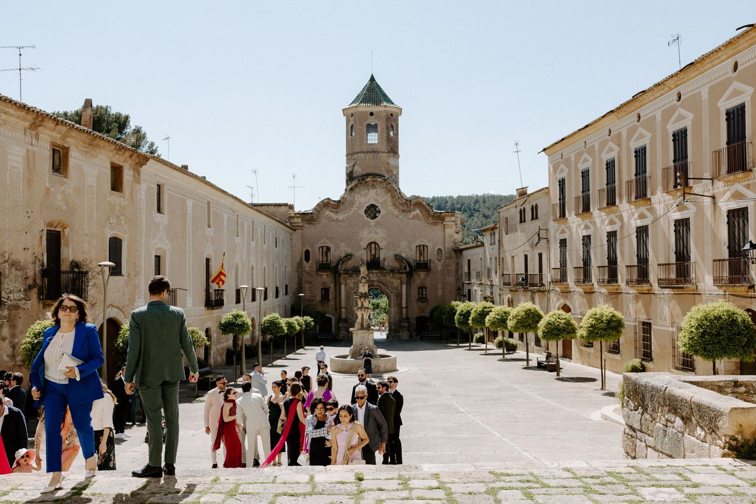 Panoramic view of a historic town square with stone buildings and gathering crowds.
