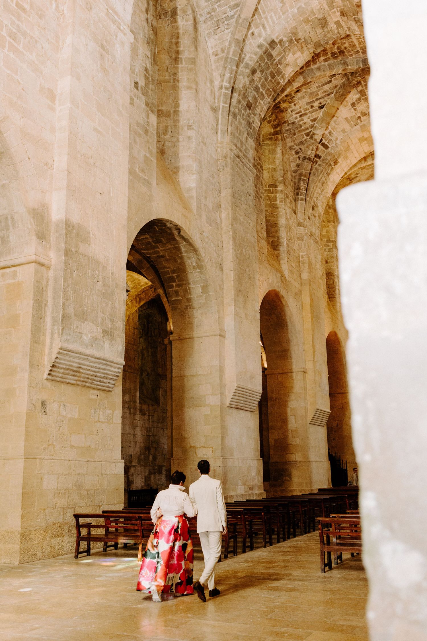 Stone arched hallway in historic building with wooden benches along the walls.