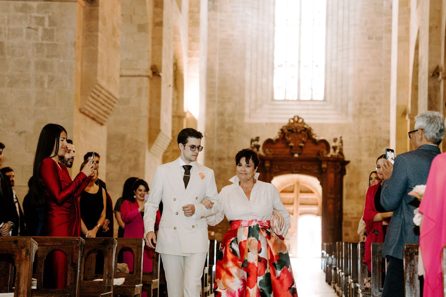 Interior of historic stone church with visitors gathered near ornate wooden furnishings.