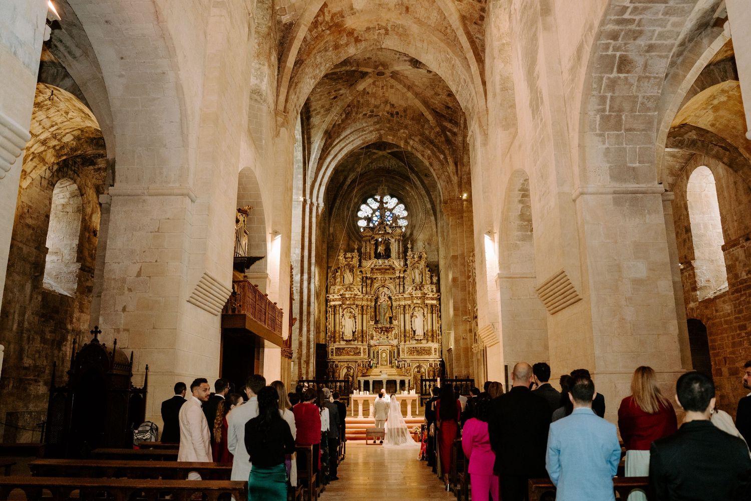 View down the center aisle of a historic cathedral with vaulted ceilings during a wedding ceremony.