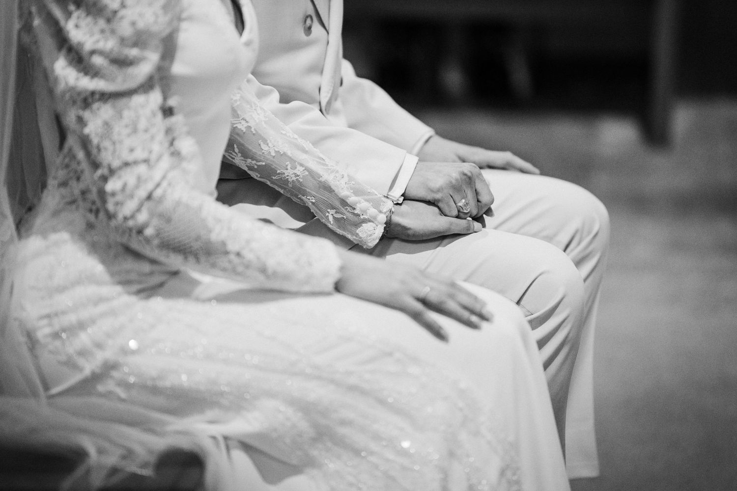 Black and white detail shot of hands resting on white wedding attire during ceremony.