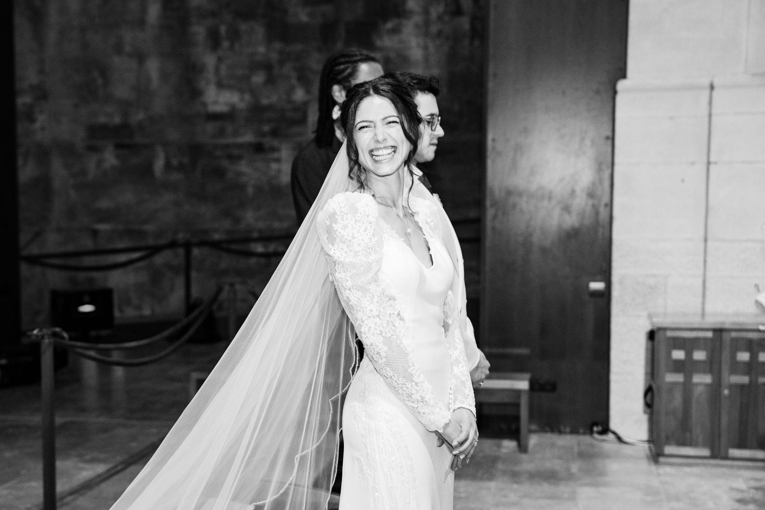 Black and white portrait of someone in an elegant lace wedding gown with flowing veil.
