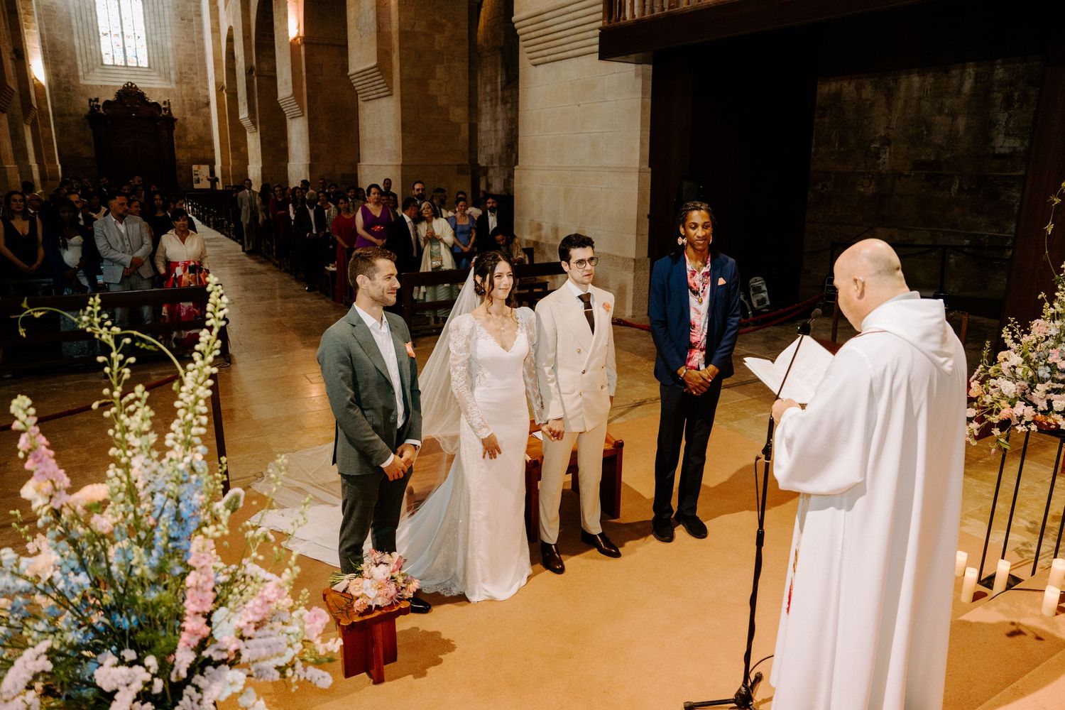 Wedding ceremony in progress with priest officiating in front of floral arrangements in historic church.