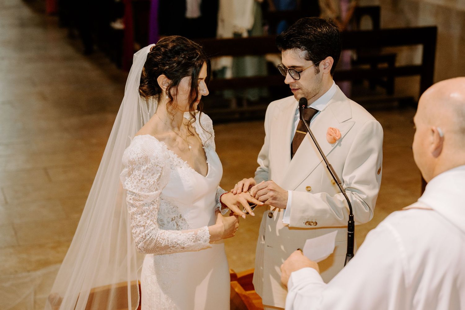 Exchange of rings during wedding ceremony with priest officiating in ornate church setting.