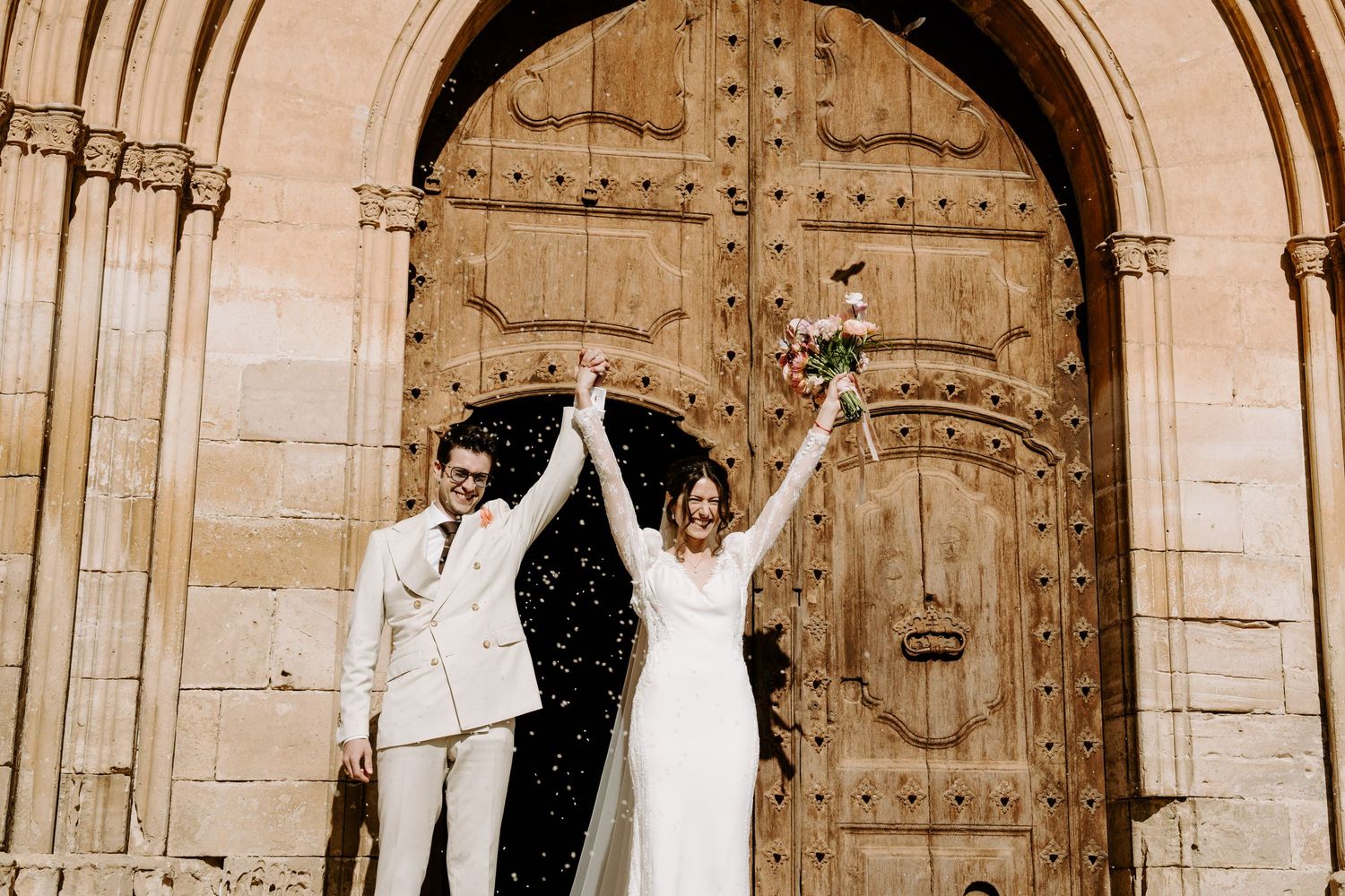 Newlyweds pose outside historic church doors with ornate stone archways.