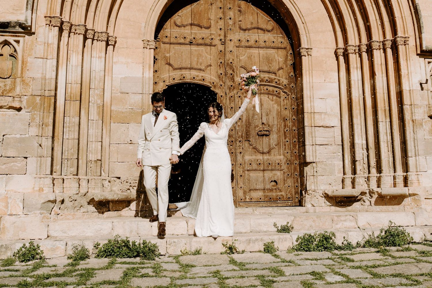 Sepia-toned wedding portraits in front of massive medieval church doors.