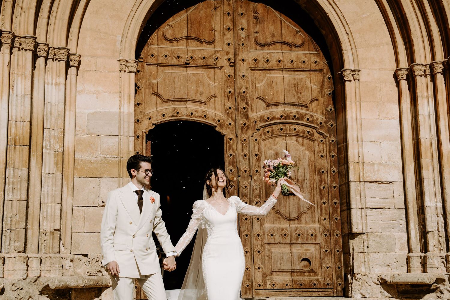 Wedding couple celebrates outside ancient stone church with architectural details.