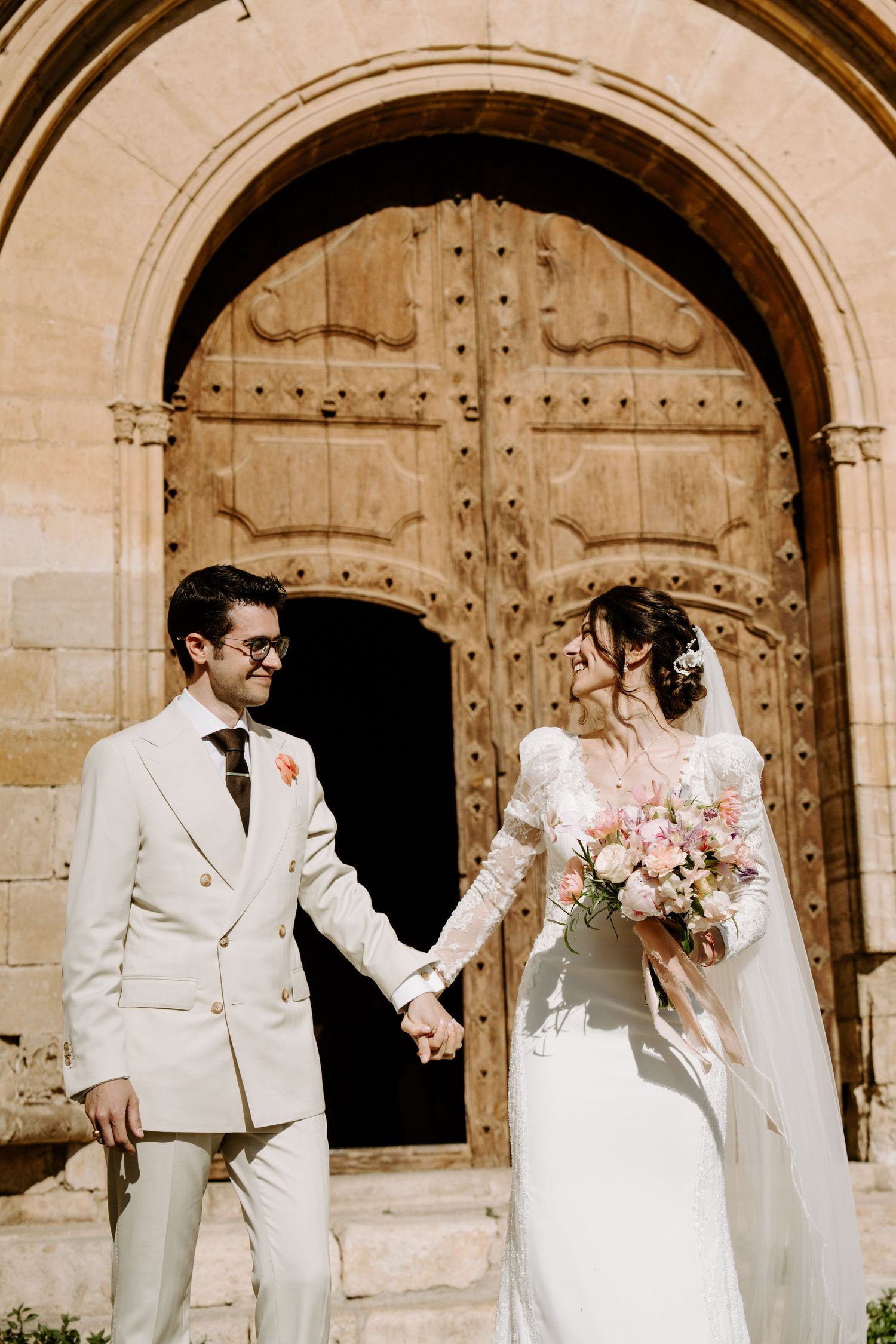 Wedding couple shares joyful moments in front of ornate church doorway.
