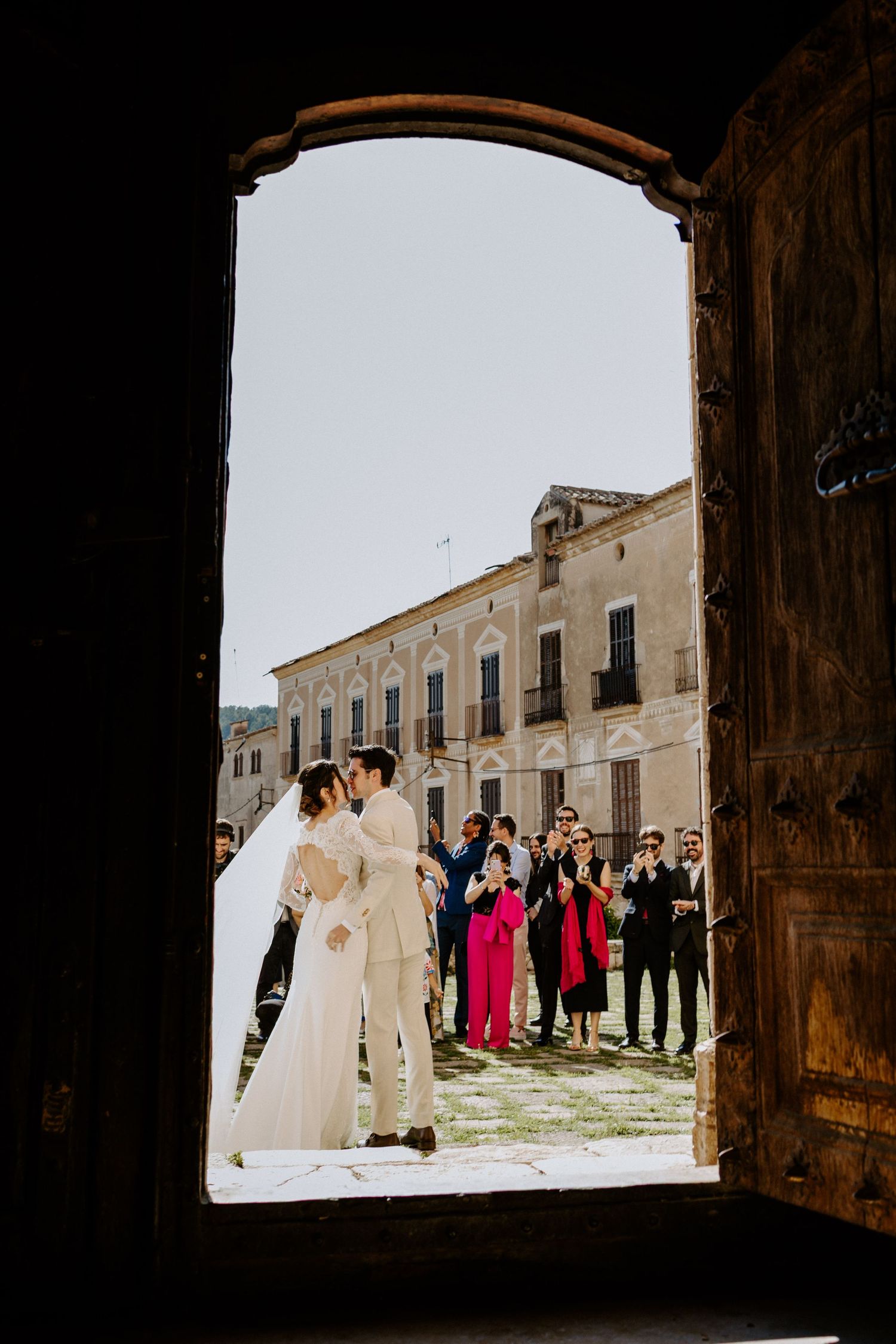 Wedding party and guests gather in church courtyard for group photos.