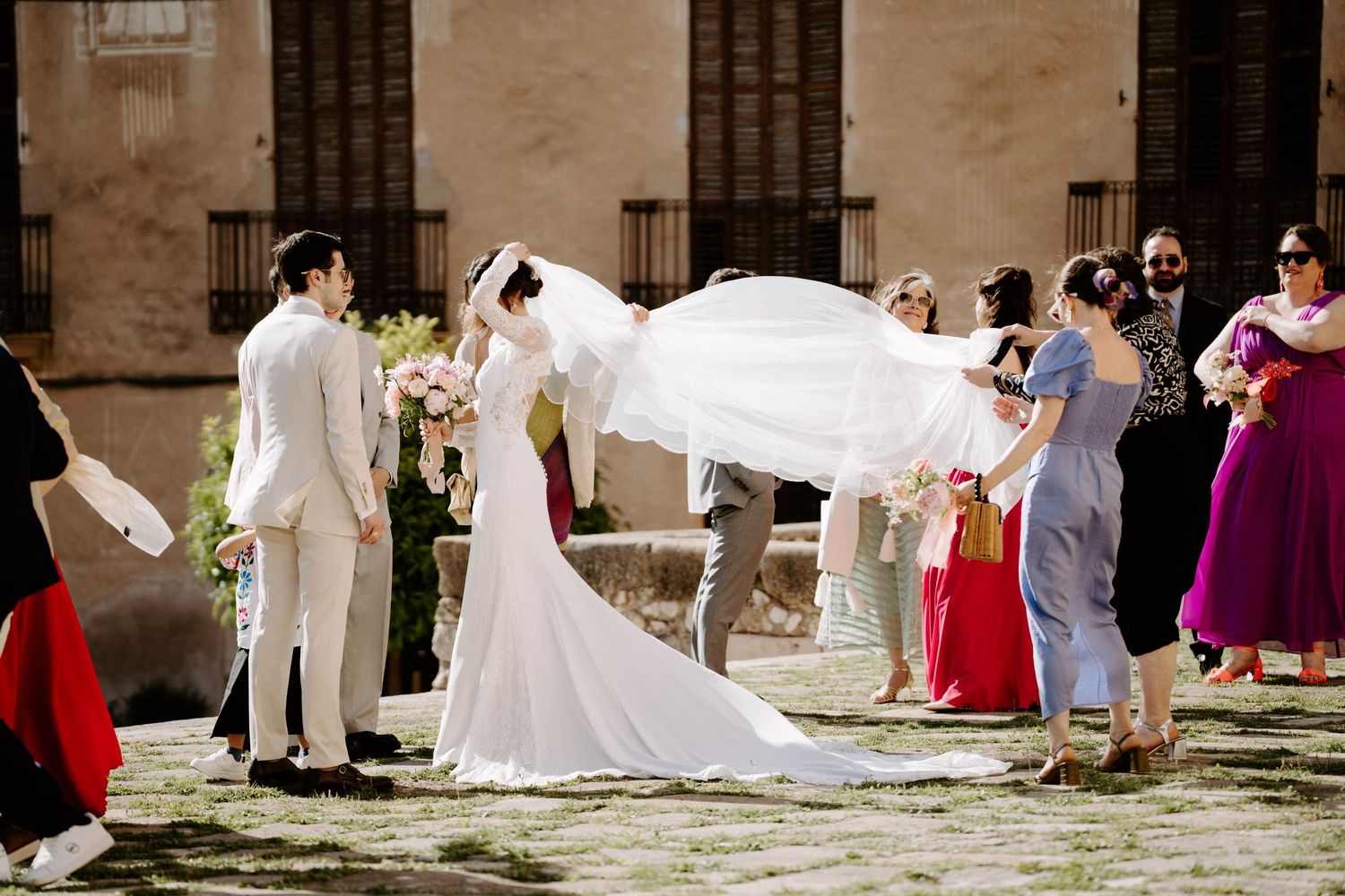 Wedding guests lined up along stone church wall in formal attire.