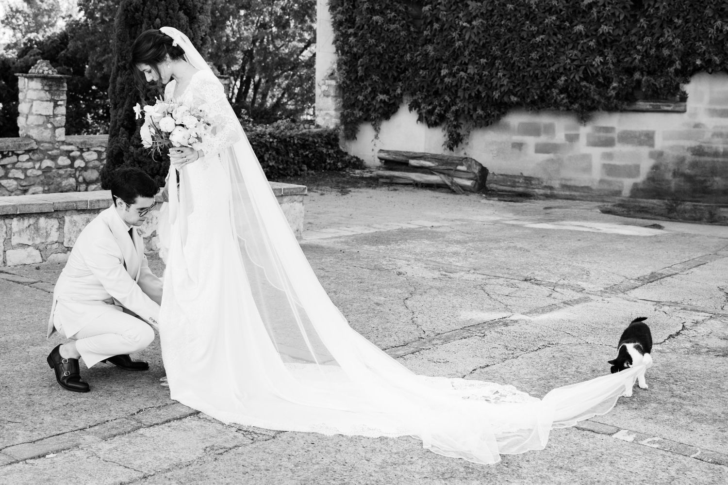 Long flowing white wedding dress train trailing across stone courtyard.