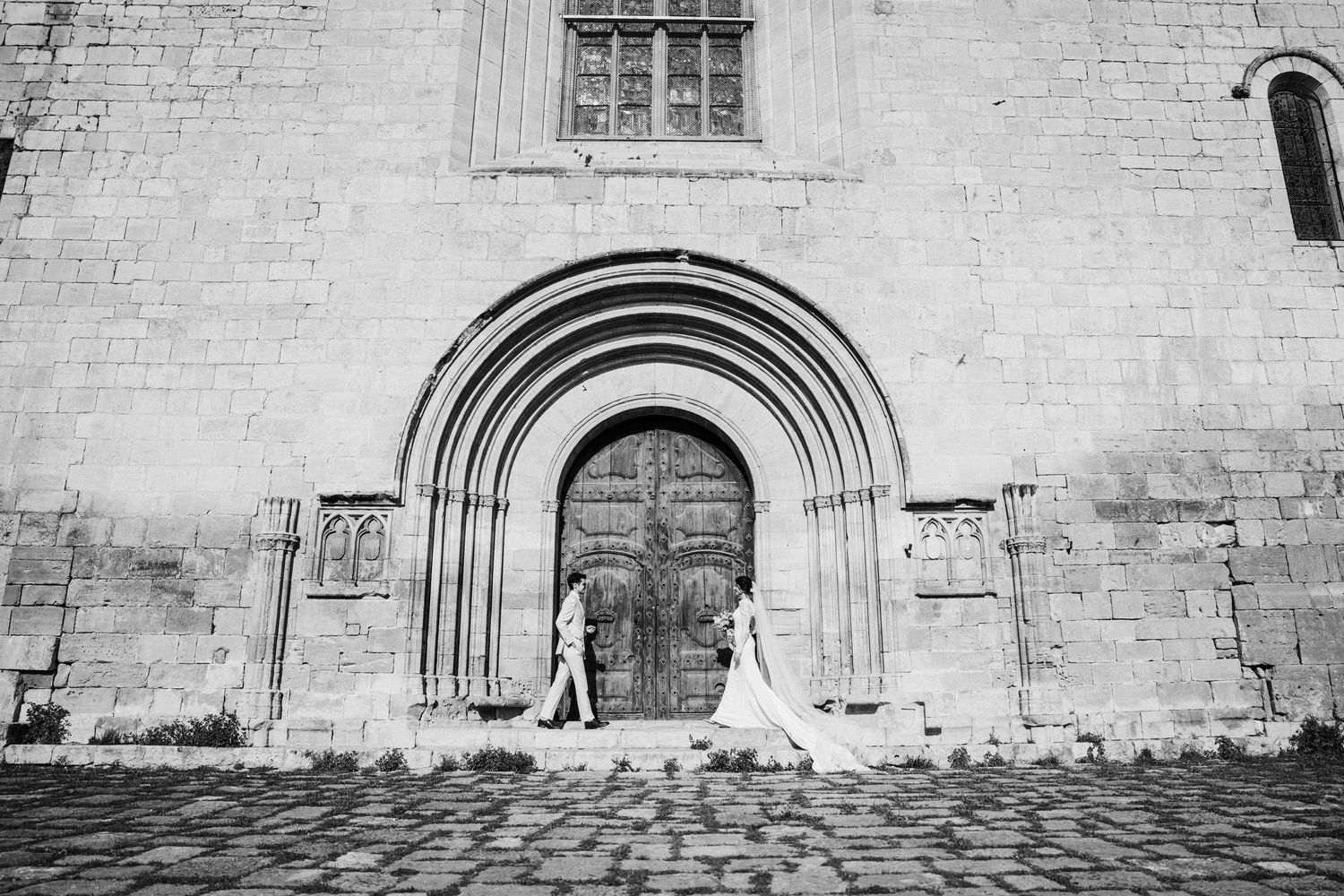 A panoramic view of a historic stone church exterior with arched doorways.