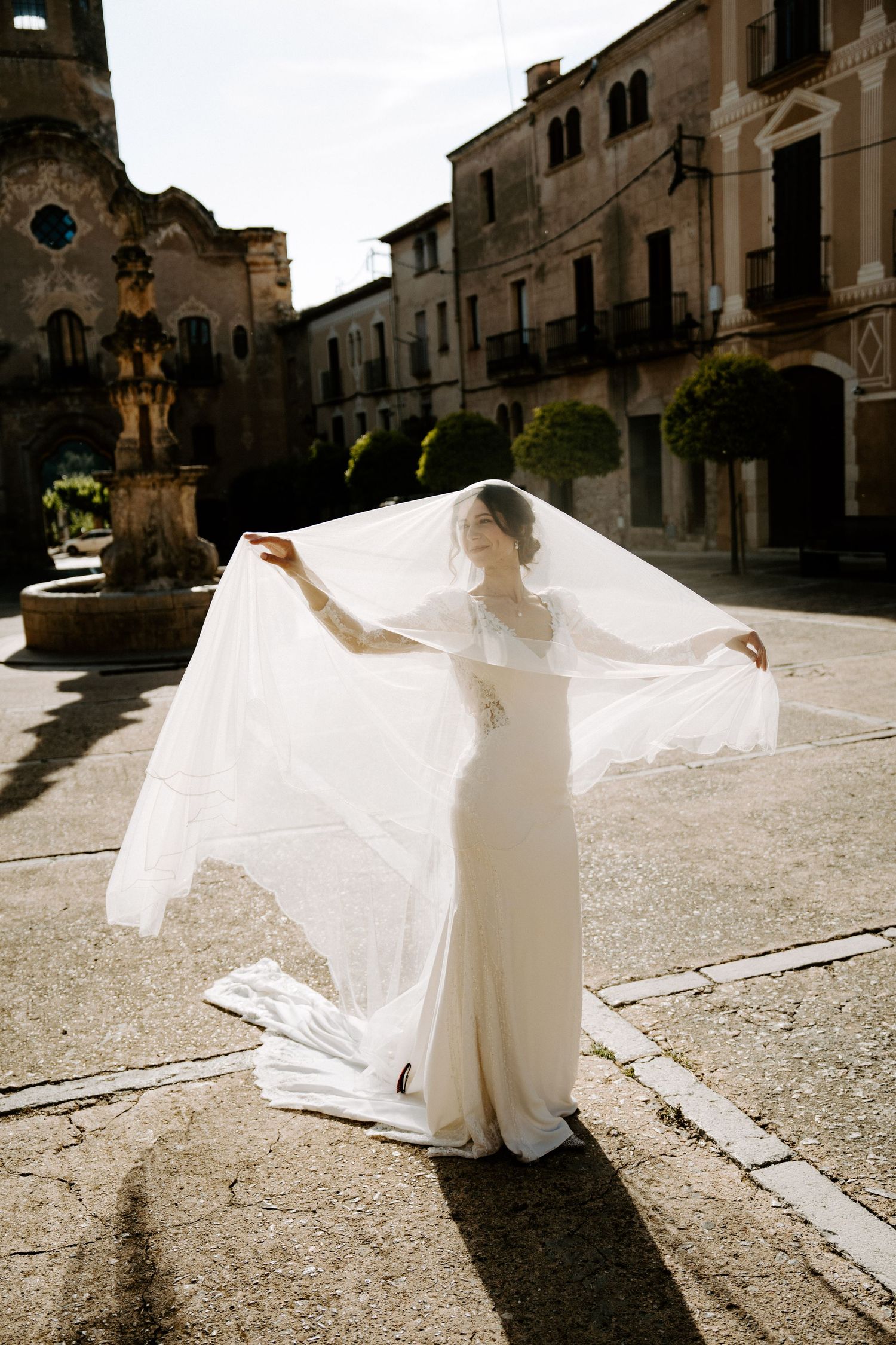 A bride twirls in a flowing white dress in a sunlit Italian plaza.