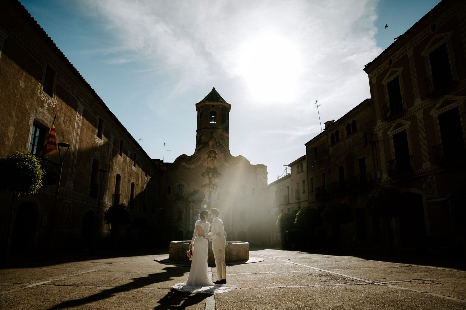 Dramatic silhouette of historic church architecture against a sunlit sky with stone buildings in foreground.