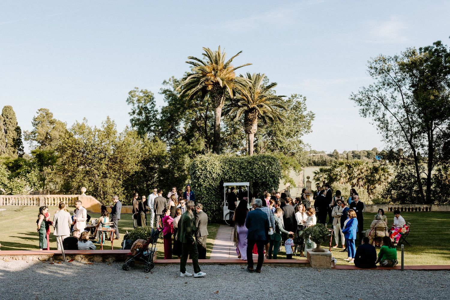 Wedding guests gathered on a lawn surrounded by palm trees and historic architecture.