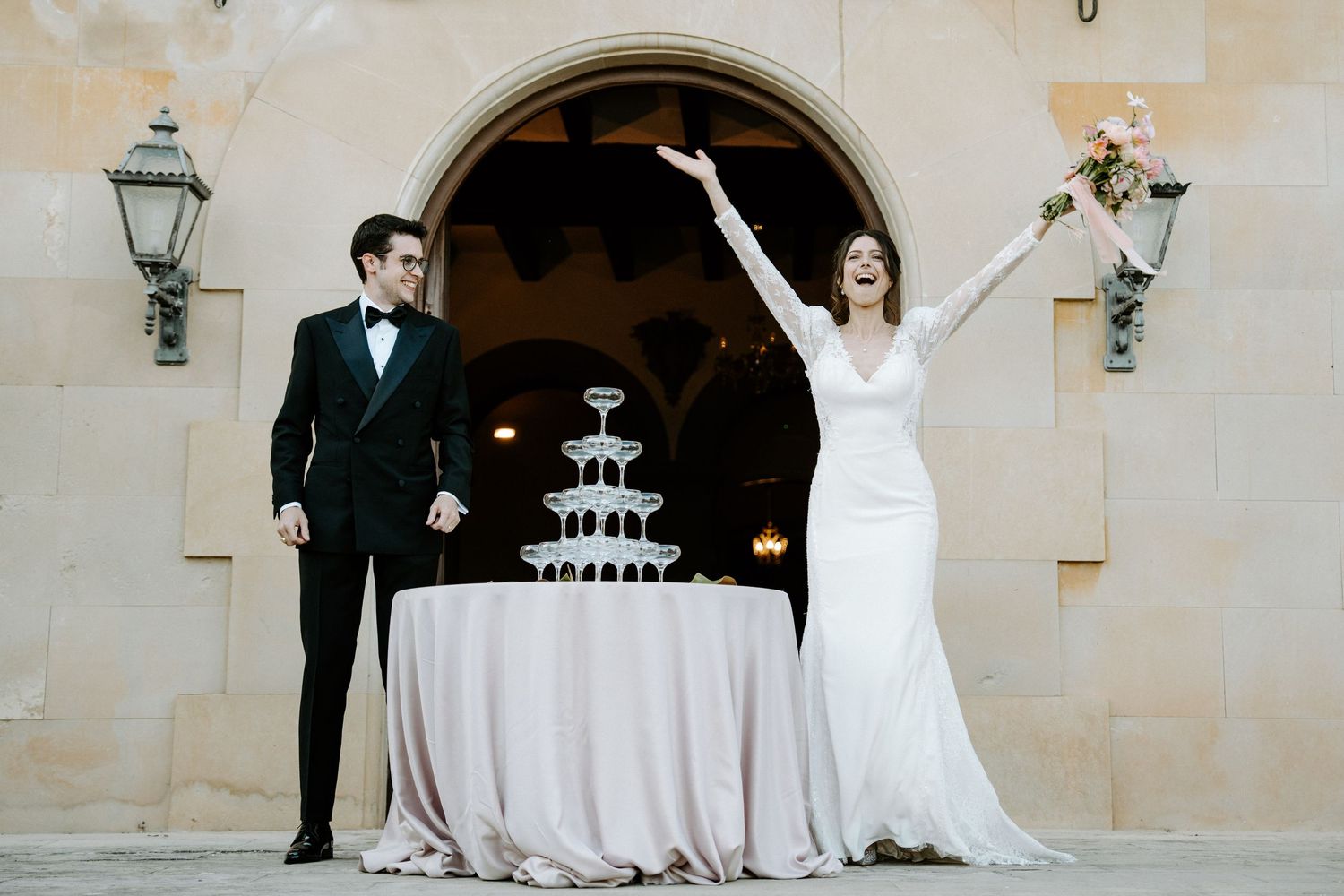 Elegant wedding cake display with champagne tower under ornate stone archway.
