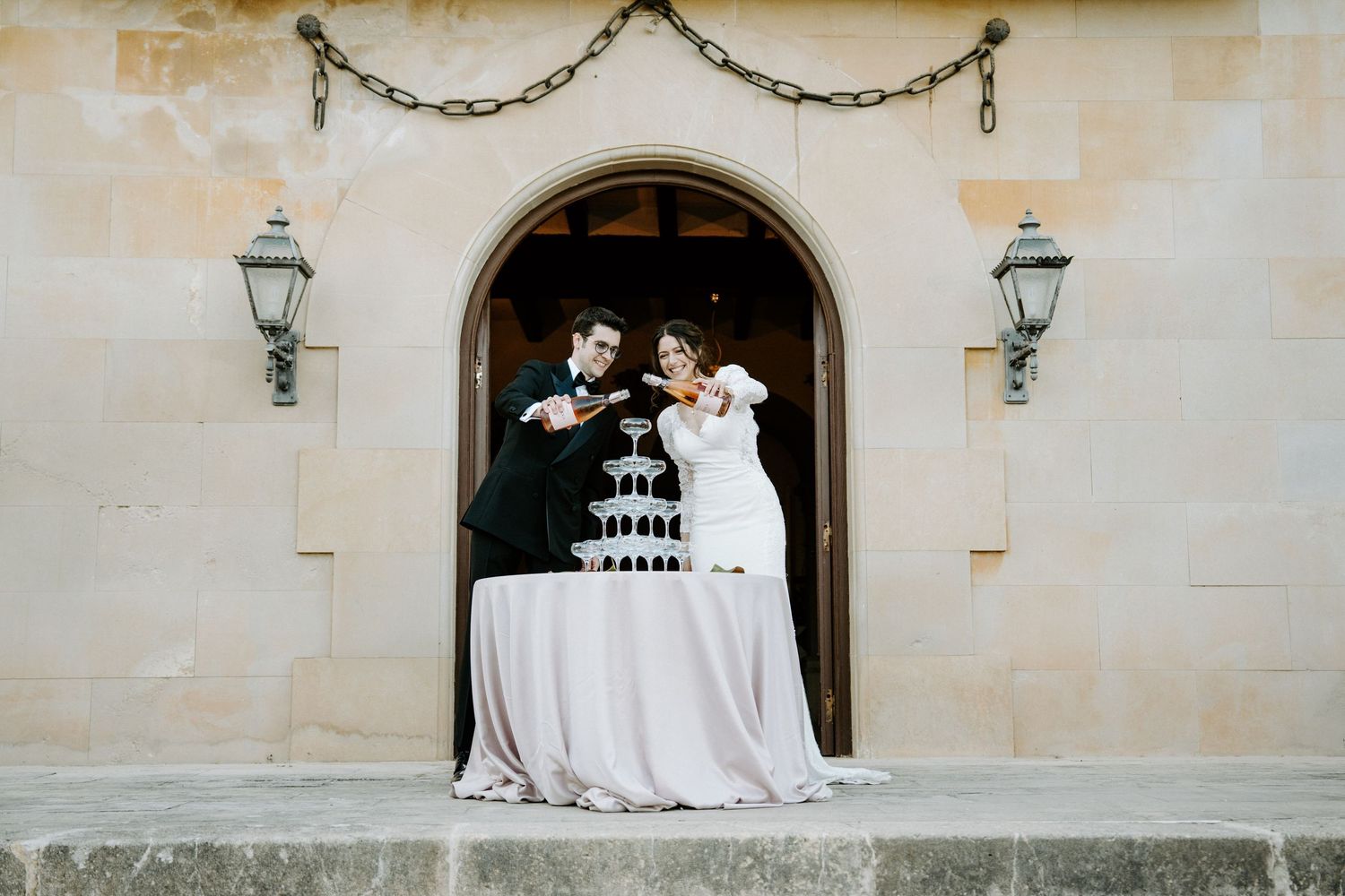 Newlyweds pour champagne into a tower of glasses at their wedding reception.