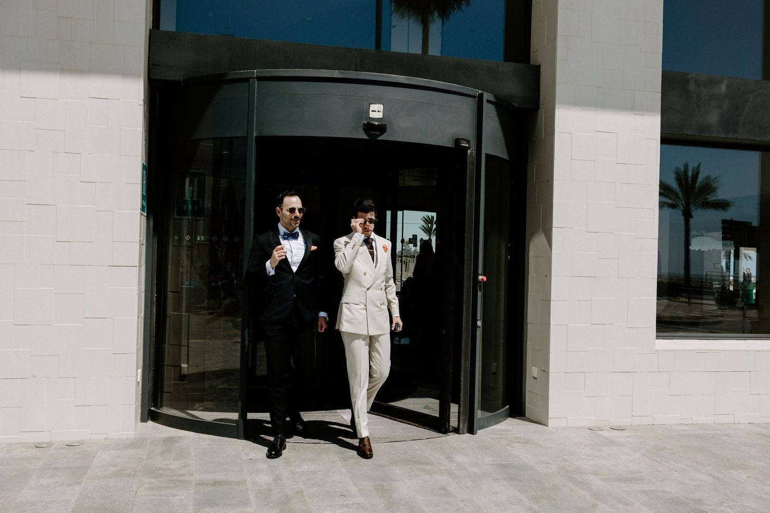 Modern white building exterior with glass doors and palm trees in the background.