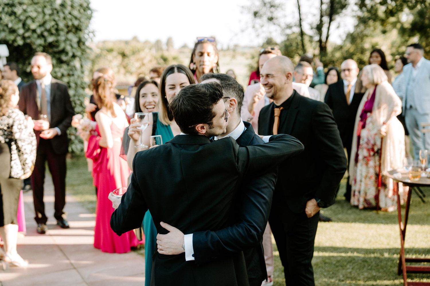 Wedding guests gather outdoors in formal attire during a sunny celebration.